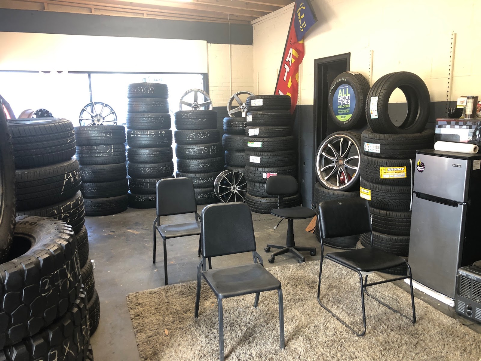 Piedmont Tires — interior showroom with stacked new tires, wheel display, chrome rims, and an All Credit Types Welcome banner