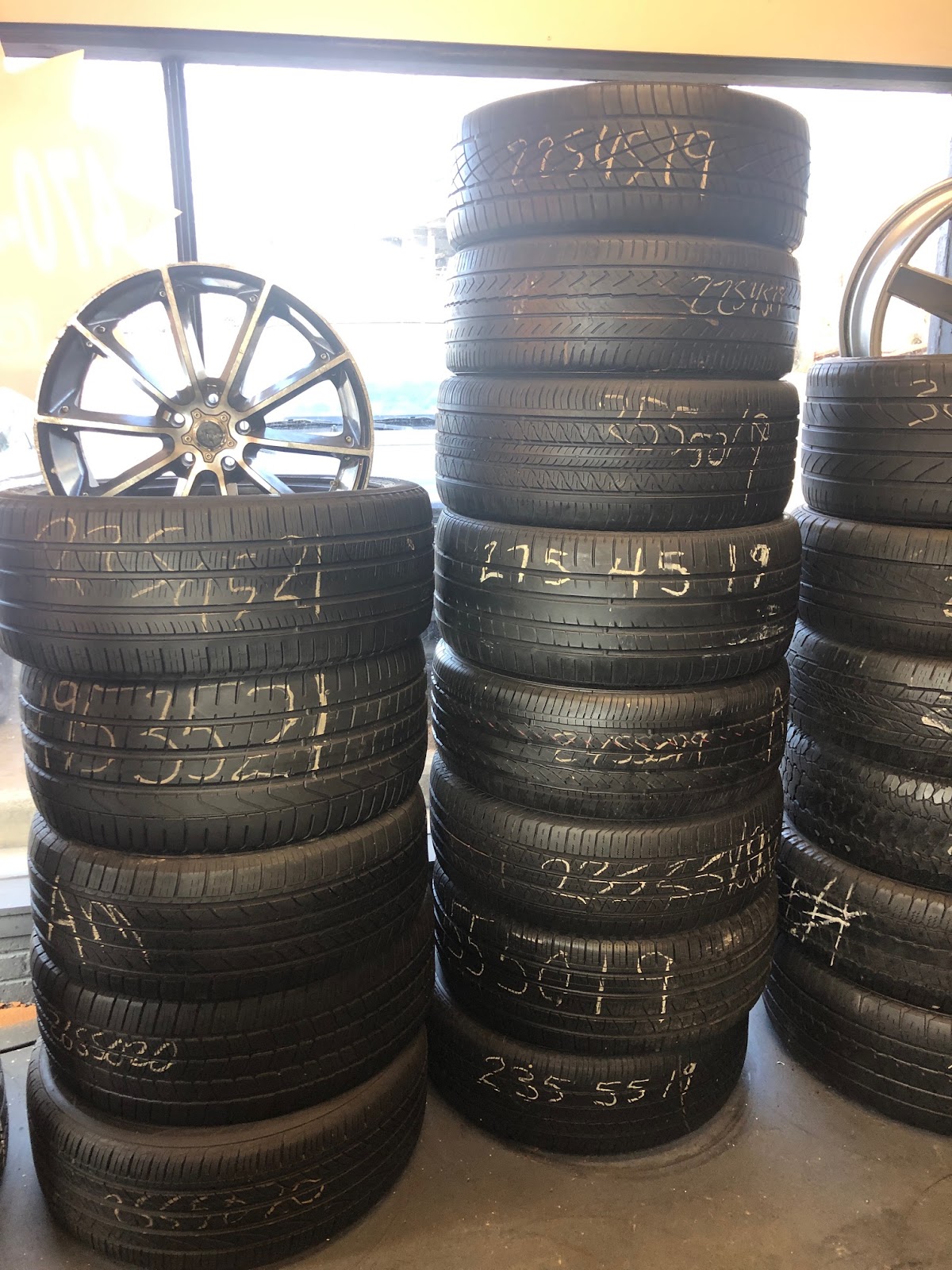 Piedmont Tires — stacks of used tires with chalk-written sizes alongside a chrome multi-spoke wheel display